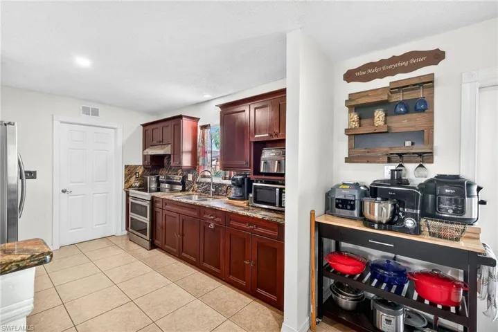 Kitchen featuring stainless steel appliances, light stone countertops, light tile patterned flooring, tasteful backsplash, and under cabinet range hood