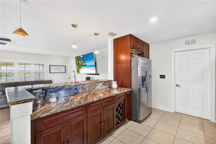Kitchen featuring dark stone counters, stainless steel fridge, pendant lighting, a peninsula, and a kitchen breakfast bar