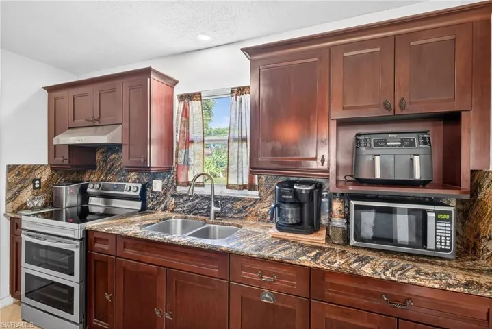 Kitchen featuring stainless steel appliances, tasteful backsplash, dark stone counters, under cabinet range hood, and a textured ceiling