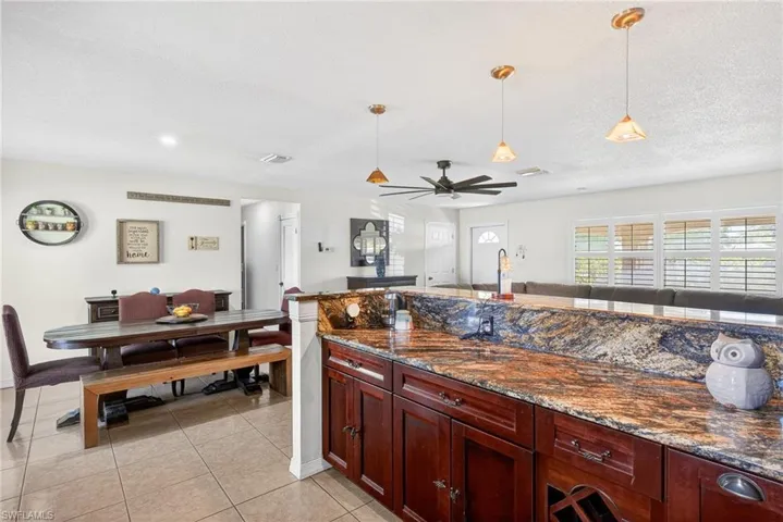 Kitchen with open floor plan, dark stone counters, decorative light fixtures, ceiling fan, and a textured ceiling