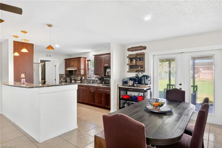 Kitchen featuring dark stone counters, a textured ceiling, stainless steel appliances, hanging light fixtures, and a peninsula