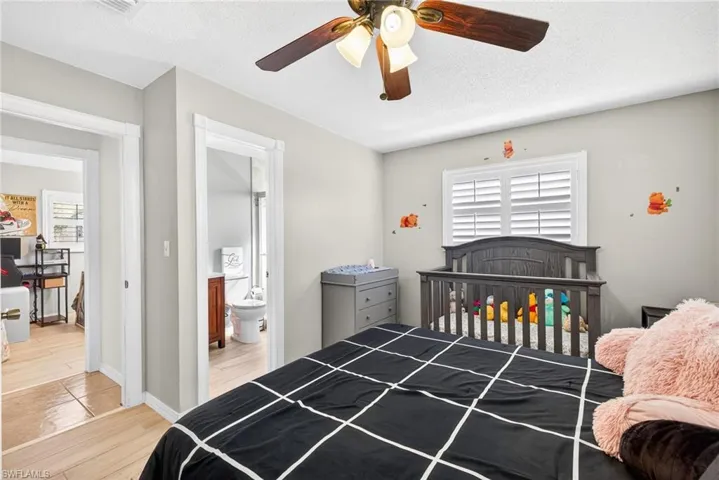 Bedroom featuring a crib, a textured ceiling, light wood-style flooring, ensuite bath, and a ceiling fan