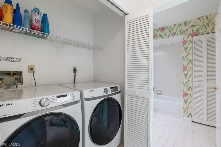 Dedicated laundry area featuring washer and dryer, storage area, white walls, and a louvered bi-fold door.