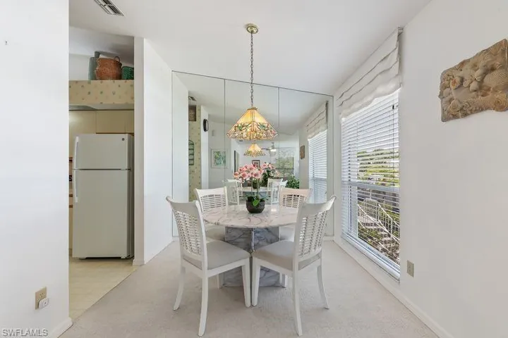 Dining area featuring a full-height mirrored wall, a window with horizontal blinds, and carpet flooring.