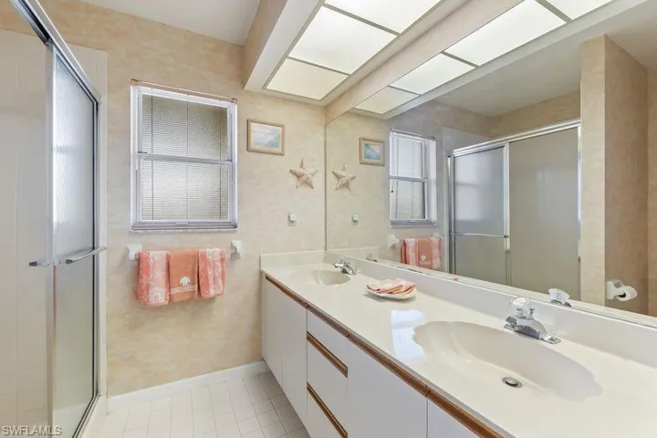 Bathroom featuring a dual-sink vanity with white cabinetry, a large mirrored wall, and walk-in shower.