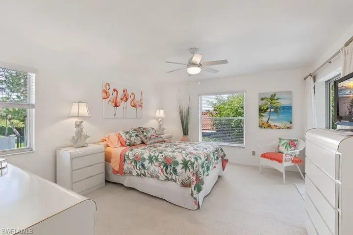 Primary bedroom featuring multiple windows, a ceiling fan with integrated lighting, neutral carpeting, ensuite bath, and slider door out to the screened lanai.