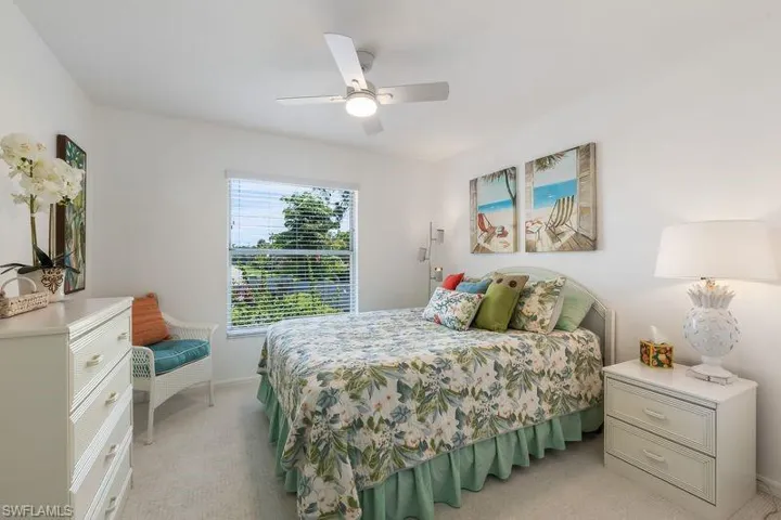 Bright bedroom featuring a new ceiling fan, large window with blinds, and light-toned carpet flooring.