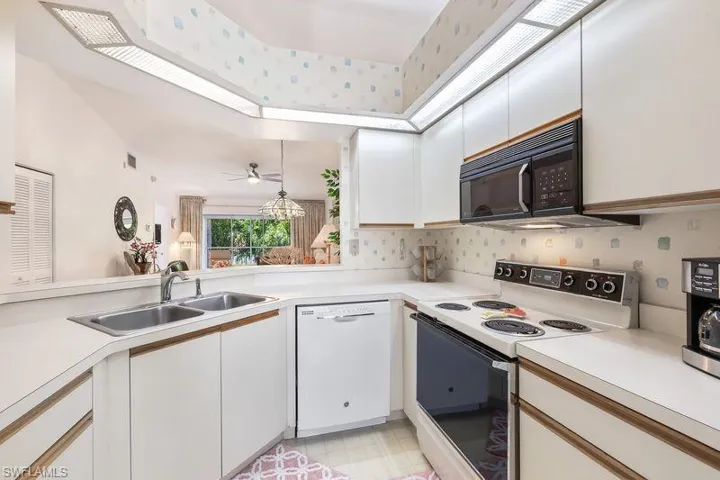 Kitchen featuring white cabinetry with wood-finish trim, a double basin stainless steel sink, and white countertops.