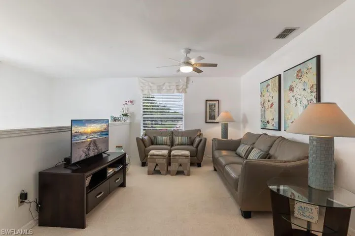 Carpeted living area featuring a new ceiling fan, window with blinds, and white walls.