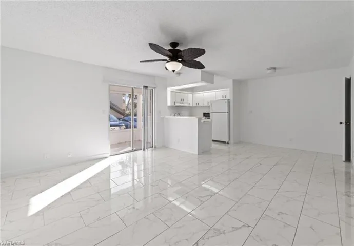 Unfurnished living room featuring a ceiling fan, light marble finish flooring, and a textured ceiling