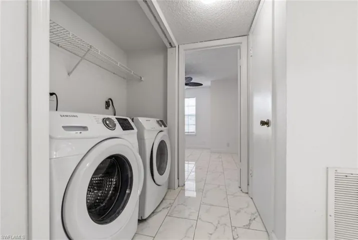 Laundry area with a textured ceiling, light marble finish floors, and washer and dryer