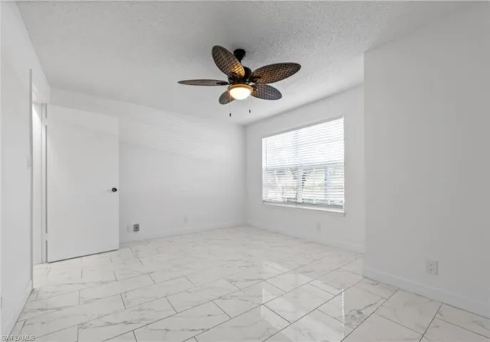 Unfurnished room with light marble finish flooring, a ceiling fan, and a textured ceiling
