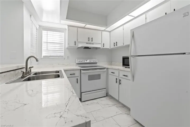 Kitchen featuring white appliances, white cabinetry, and light stone countertops