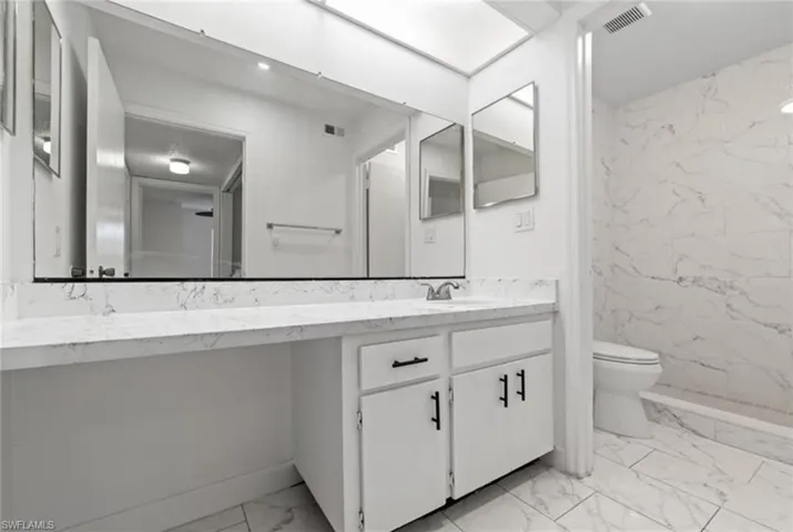 Full bath featuring light marble finish floors, vanity, and a marble finish shower