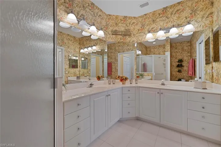 Bathroom with wallpapered walls, a stall shower, double vanity, light tile patterned flooring, and a closet