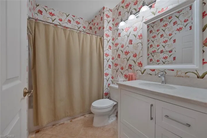 Full bath with wallpapered walls, vanity, and light tile patterned floors