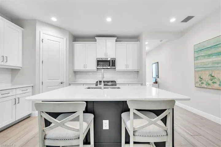 Kitchen featuring a large central island with a white countertop and dark base cabinetry, white upper and lower cabinetry, a stainless steel microwave, and wood-finish flooring