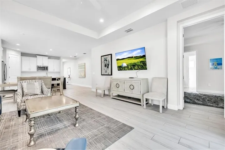 Open concept living space featuring recessed lighting, a tray ceiling, light wood-finish flooring, and white kitchen cabinetry with stainless steel appliances