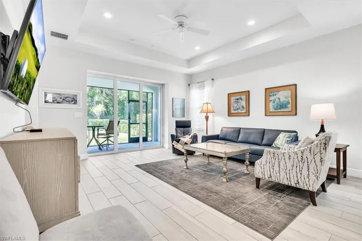 Living area featuring light wood-finish flooring, a tray ceiling with recessed lighting and a ceiling fan, and sliding glass doors leading to a screened patio