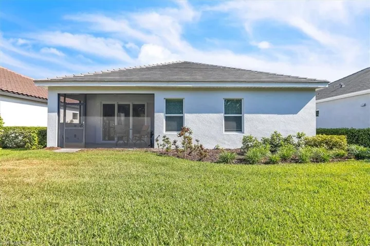 Rear exterior featuring a screened patio, sliding glass doors, white stucco finish, a tiled roof, and landscaped garden beds