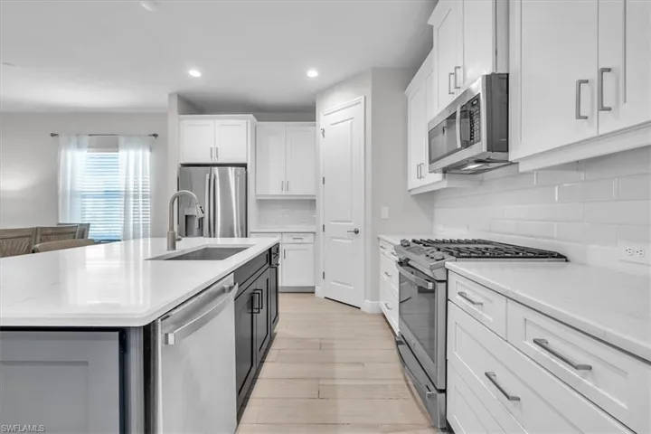 Spacious kitchen featuring an extended island with a built-in sink and dishwasher, white shaker cabinetry, stainless steel appliances, and light wood-finish flooring