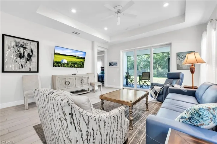 Spacious living area featuring light-toned flooring, tray ceiling, recessed lighting, and a ceiling fan
