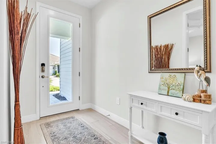 Glass-paneled entry door featuring a smart lock system, light wood-finish flooring, white baseboards, and neutral wall paint