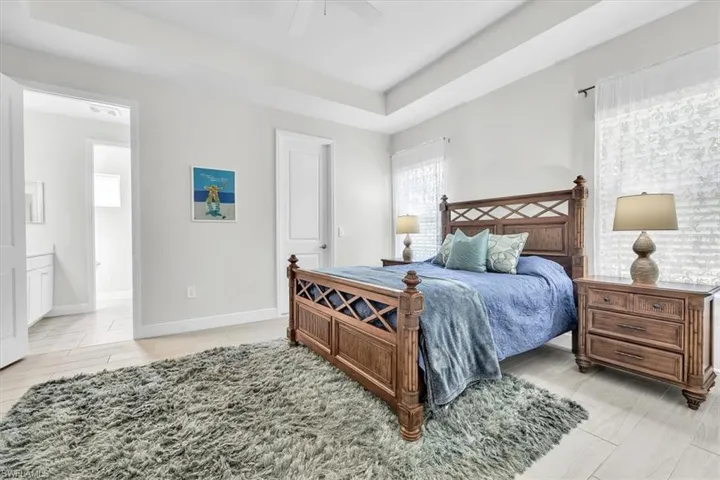 Spacious bedroom featuring wood-finish tile flooring, a tray ceiling, and white trim throughout