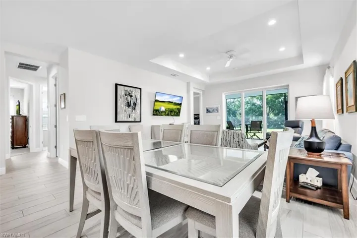 Open-concept living area featuring light wood-finish flooring, a tray ceiling with recessed lighting, and a ceiling fan