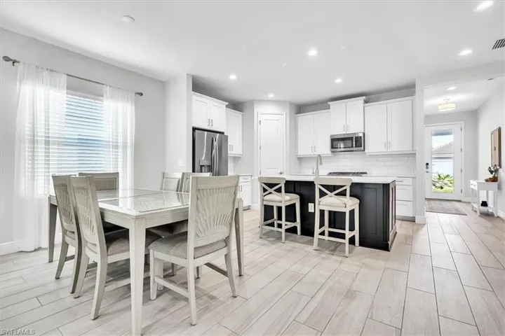 Open-concept living space featuring wood-look tile flooring, white shaker cabinetry, a dark kitchen island with seating, stainless steel appliances, and recessed lighting