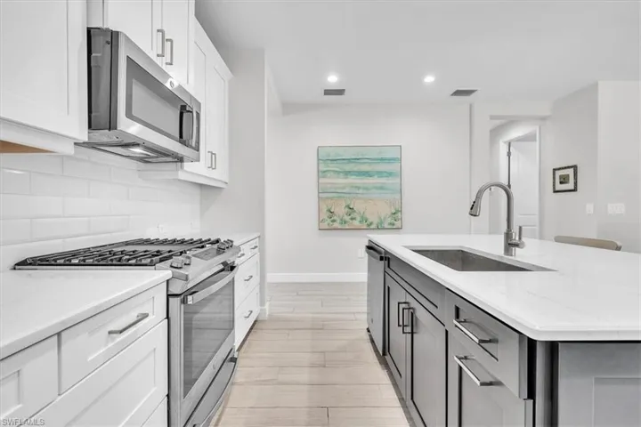 Kitchen featuring white shaker cabinetry, stainless steel appliances, a subway tile backsplash, and light wood-finish flooring