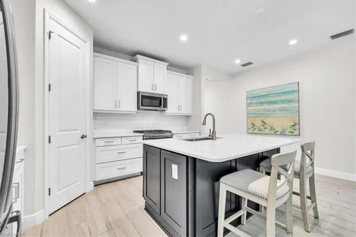 Kitchen featuring a contrasting dark island with an integrated sink, white cabinetry with silver hardware, stainless steel microwave, and wood-finish flooring