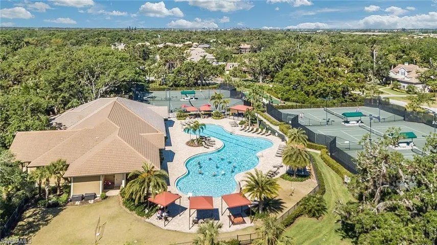 Resort-style pool area featuring a freeform swimming pool, multiple shaded lounging areas, and surrounding palm trees