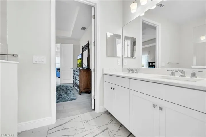 Modern vanity with dual sinks, white cabinetry, and a large wall-mounted mirror, set against white walls and marble-style floor tiling