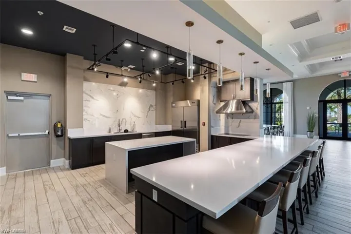 Exhibition Kitchen featuring  pendant lighting, stainless steel built in fridge, light stone countertops, and black electric stovetop
