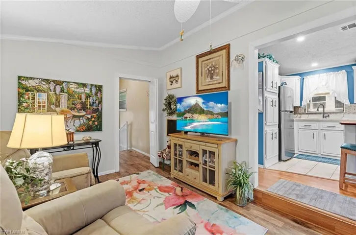 Living room with a textured ceiling, ornamental molding, and light wood-style floors