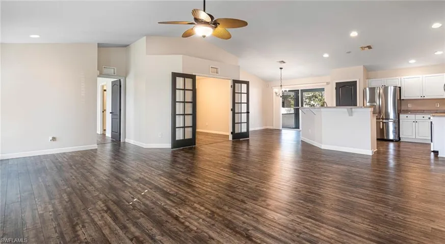 Living room featuring dark LPV floors, ceiling fan, french doors, cathedral ceilings