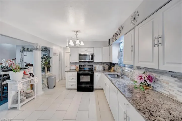 Kitchen featuring white cabinets, sink, black range with electric stovetop, hanging light fixtures, and backsplash