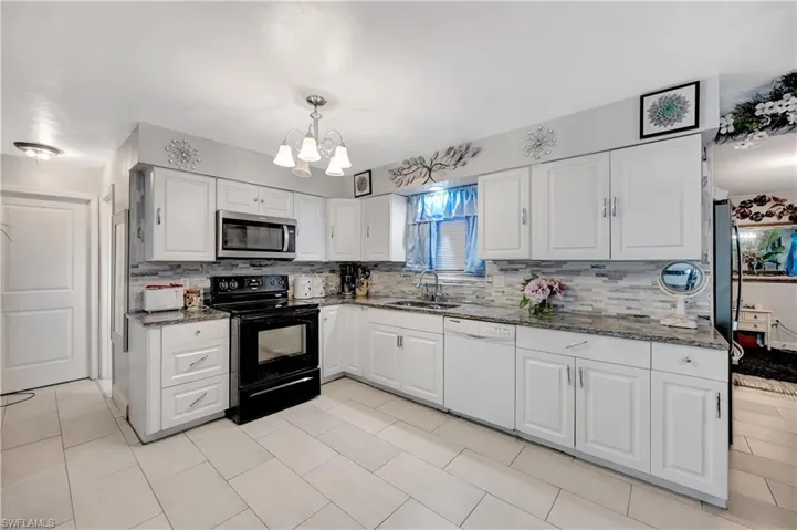 Kitchen with white cabinetry, white dishwasher, black range with electric cooktop, hanging light fixtures, and sink