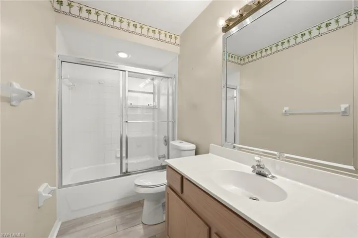 Full bathroom with vanity, hardwood / wood-style floors, shower / bath combination with glass door, and toilet