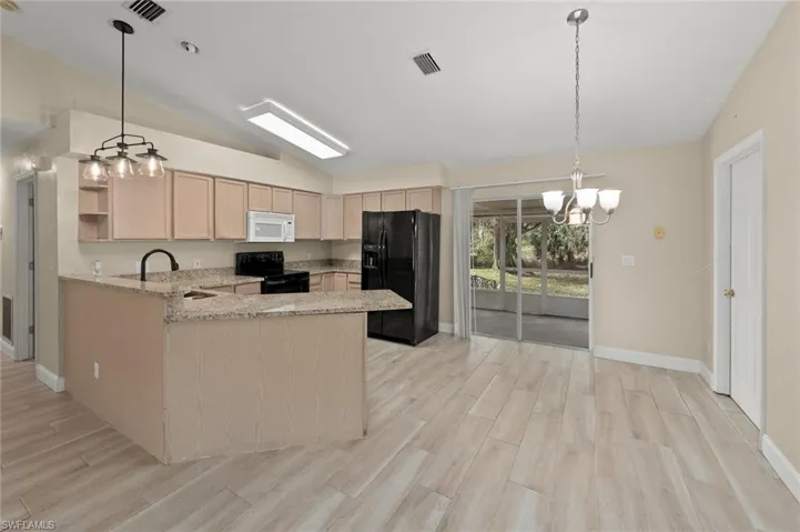 Kitchen with lofted ceiling, light brown cabinetry, kitchen peninsula, pendant lighting, and black appliances