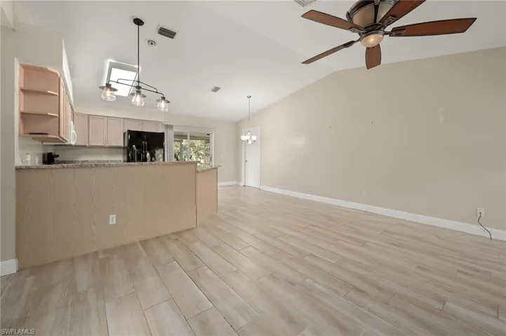 Kitchen with lofted ceiling, light brown cabinetry, black fridge with ice dispenser, and light hardwood / wood-style floors