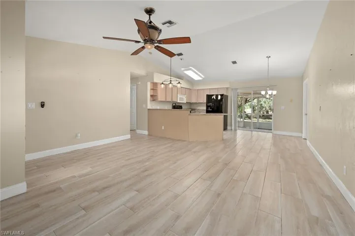Unfurnished living room featuring ceiling fan with notable chandelier, vaulted ceiling, and light wood-type flooring