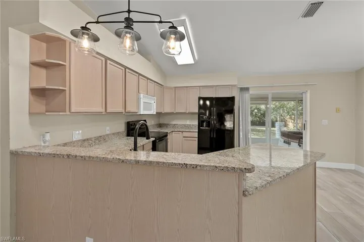 Kitchen with light stone countertops, kitchen peninsula, light brown cabinets, and black appliances