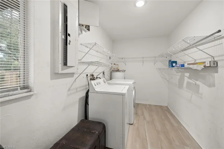 Clothes washing area featuring washing machine and clothes dryer, electric panel, and light wood-type flooring