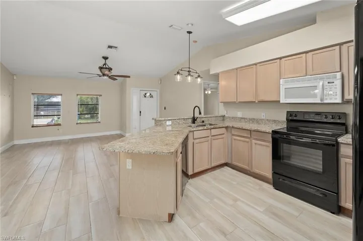 Kitchen with light brown cabinetry, sink, vaulted ceiling, kitchen peninsula, and black appliances