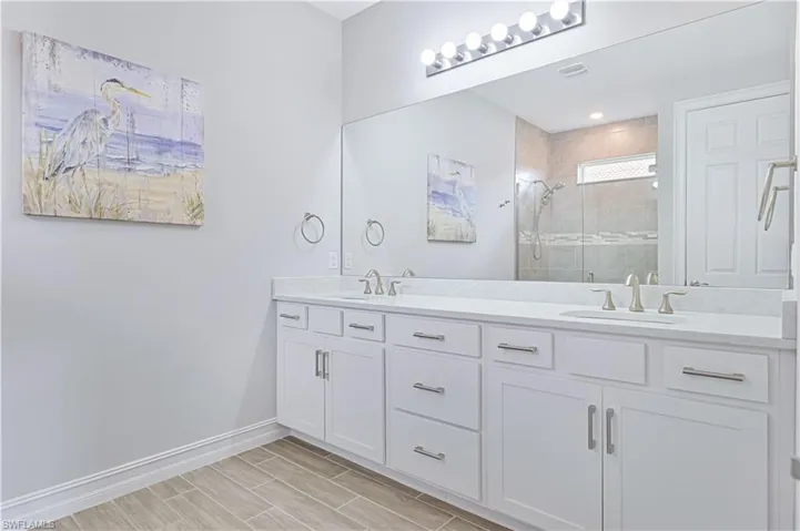 Full bathroom with double vanity, a stall shower, and baseboards