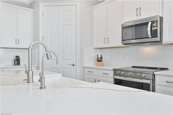 Kitchen with appliances with stainless steel finishes, white cabinetry, ornamental molding, a sink, and decorative backsplash