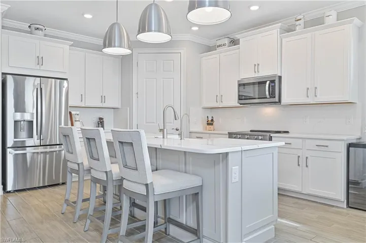 Kitchen featuring appliances with stainless steel finishes, ornamental molding, light countertops, white cabinets, and a center island with sink