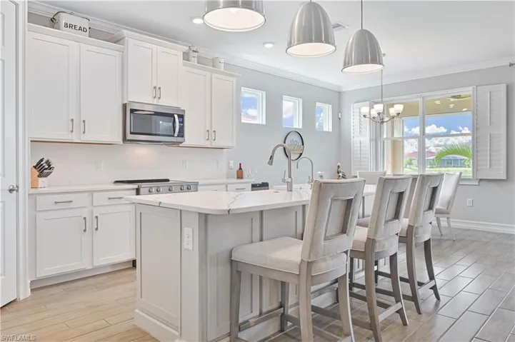 Kitchen with stainless steel microwave, crown molding, an island with sink, light wood-style floors, and white cabinetry